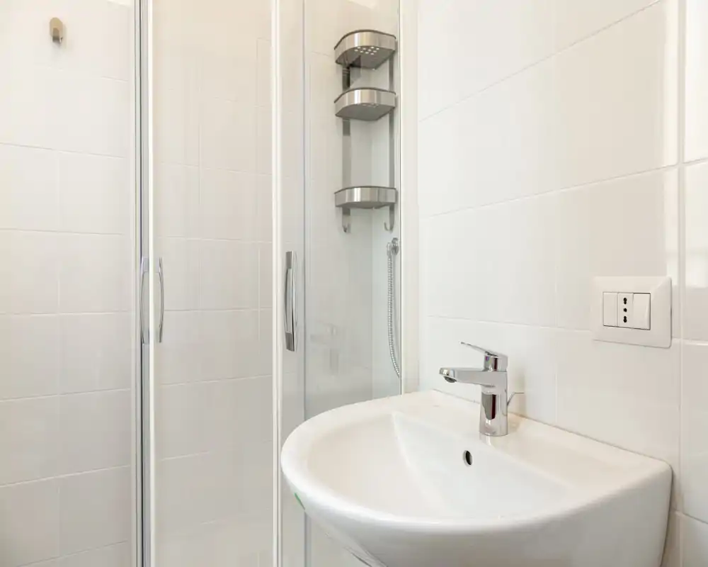Bright, modern bathroom with a wall-mounted sink and glass-enclosed shower; clean white tiles and chrome fittings provide a fresh, minimal aesthetic.