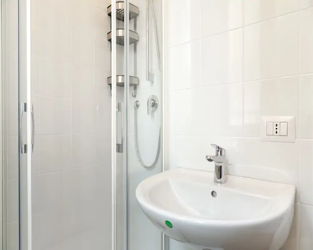 Clean, modern bathroom view showing a sink and a glass-enclosed shower with chrome fixtures and white tiles.