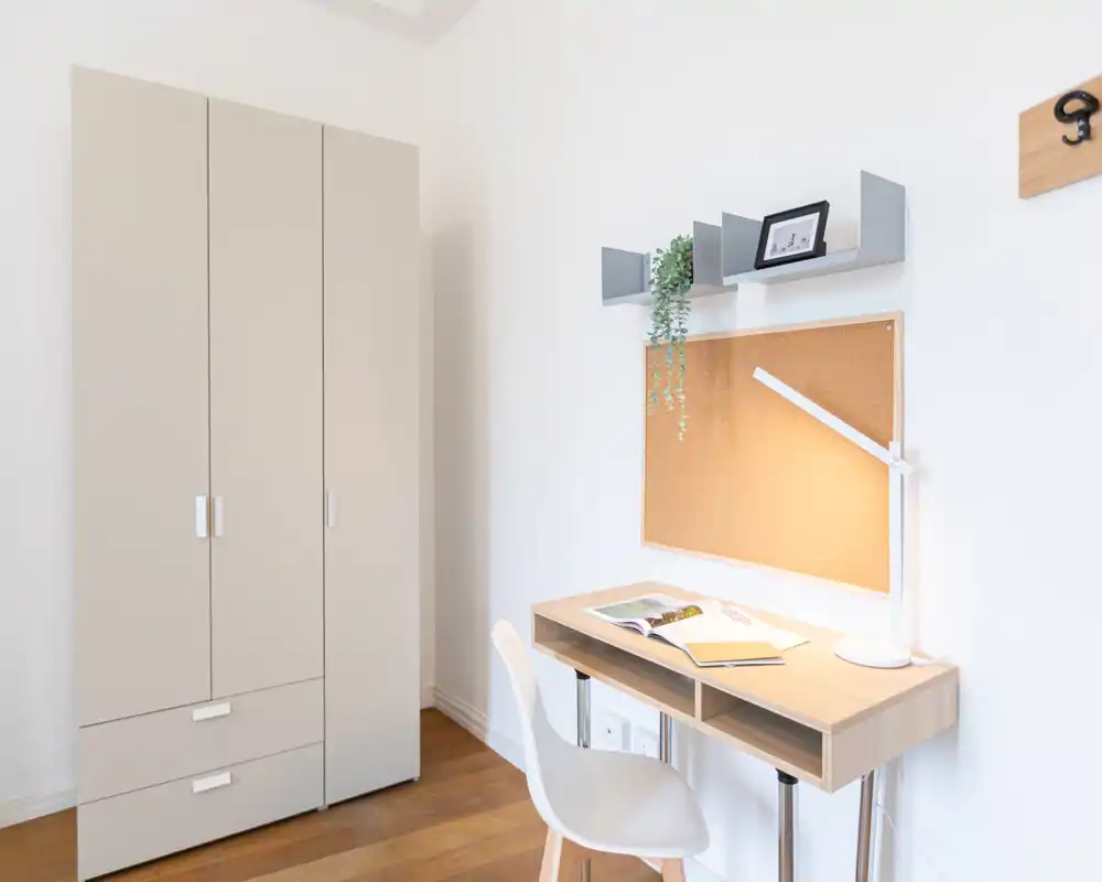Angolo camera luminoso e minimale con armadio, scrivania compatta, sedia e bacheca in sughero — ideale come angolo studio accogliente.