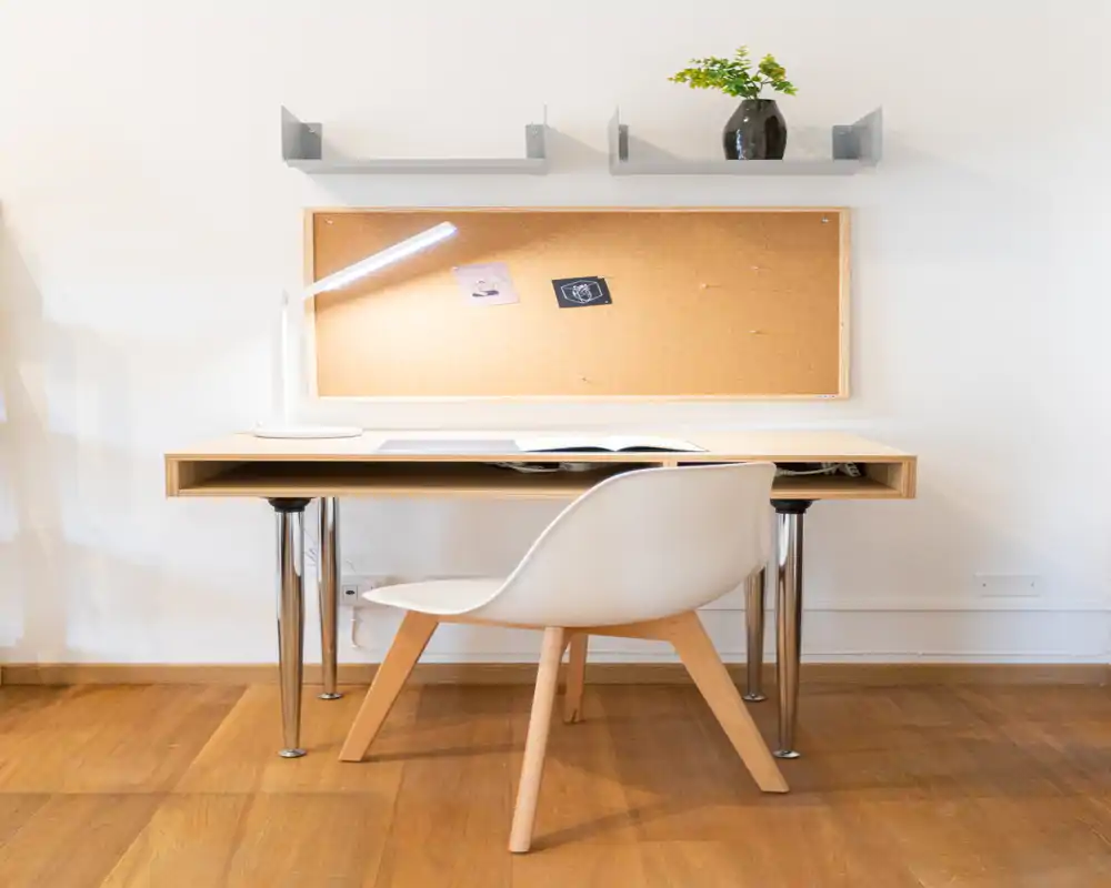 Spazio di lavoro luminoso e minimal con scrivania in legno, sedia bianca moderna, lampada e bacheca in sughero — pulito e accogliente per studiare o lavorare.