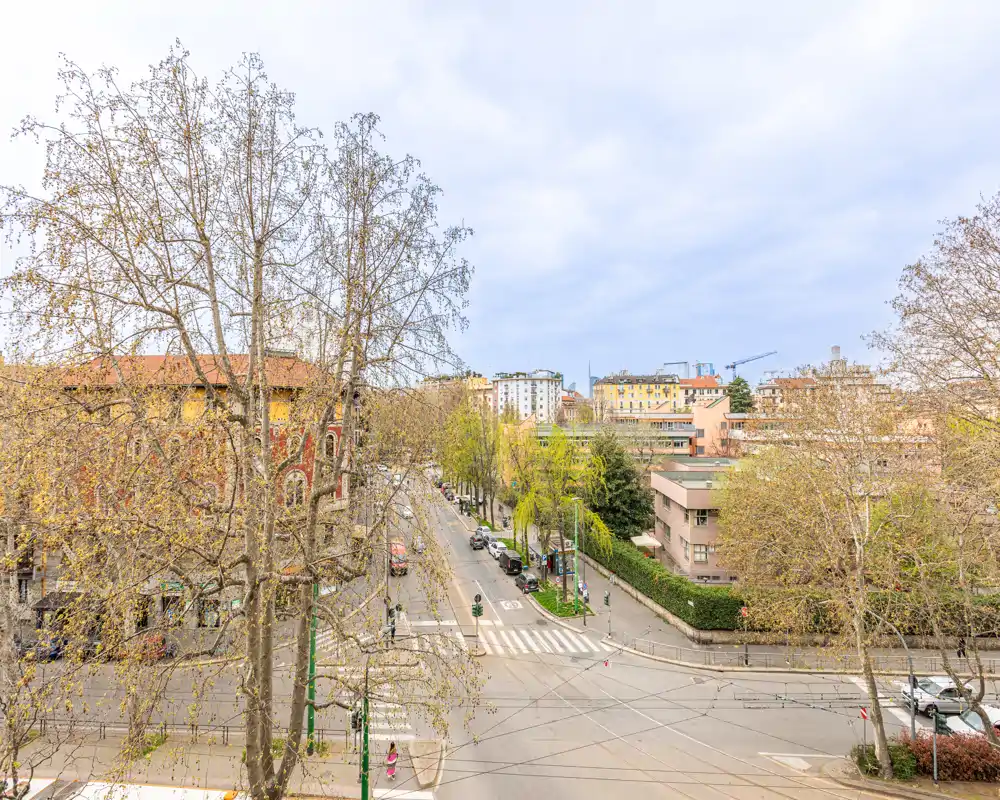 Visuale cittadina da un piano alto con alberi, attraversamento pedonale e palazzi residenziali circostanti — ideale per inserire un appartamento con bella vista.