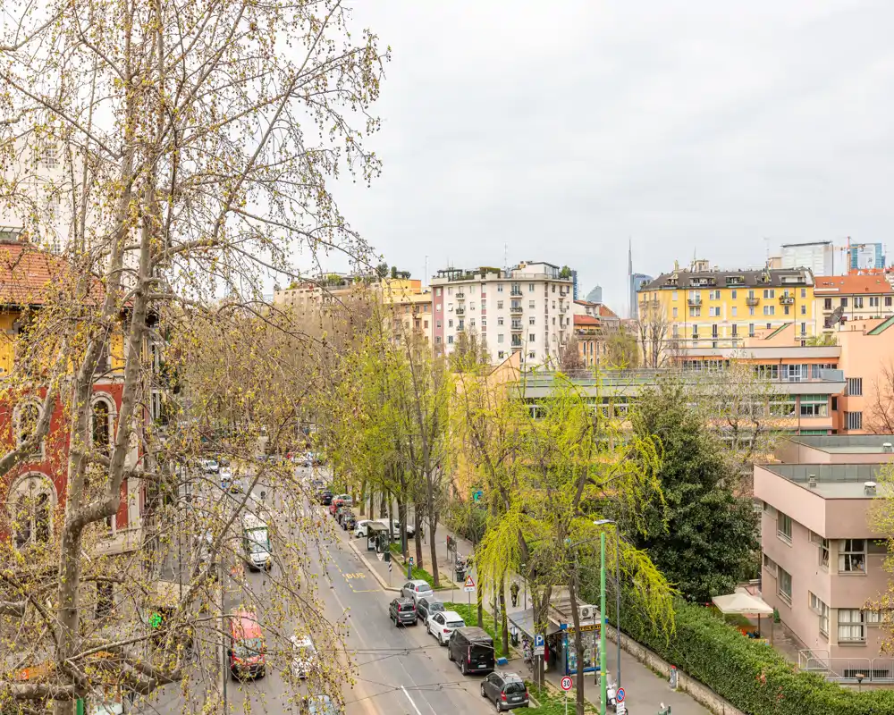 Vista urbana luminosa da un piano alto con strada alberata, auto parcheggiate e palazzi circostanti — ideale per mostrare la posizione e il quartiere nell'annuncio.