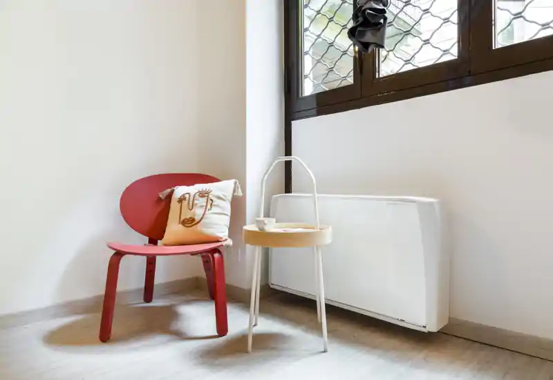 Angolo conversazione luminoso e minimale con una sedia rossa, cuscino decorativo e un piccolo tavolino rotondo accanto alla finestra — perfetto per mostrare un angolo accogliente del soggiorno.
