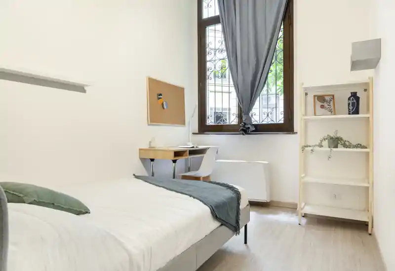 Bright, minimal single bedroom with a neatly made bed, small desk by the window and simple shelving — ideal for a student or solo renter.