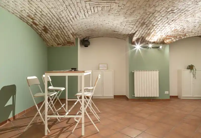 Zona giorno luminosa e di stile con soffitto a volta in mattoni, pavimento in cotto, un tavolo alto e sedie pieghevoli — perfetta per incontri informali o un angolo lavoro.