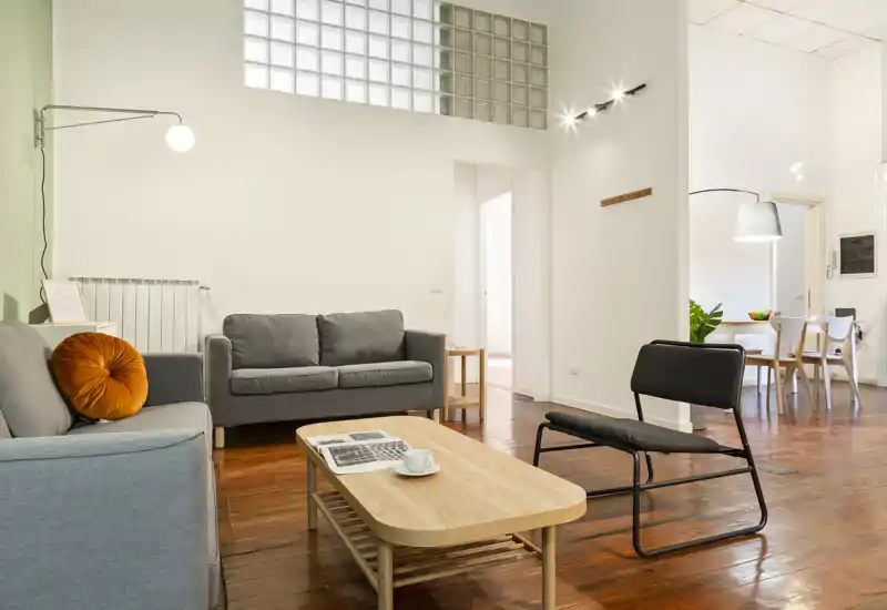 Soggiorno luminoso e di stile con divani confortevoli, tavolino basso in legno e poltrona moderna — pavimento in legno caldo e illuminazione soffusa creano un'atmosfera accogliente.