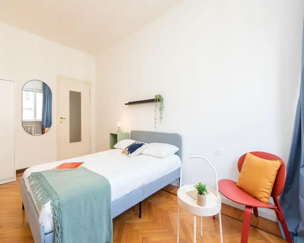 Dormitorio moderno y luminoso con cama doble completamente visible, textiles cuidados y una pequeña zona de estar junto a la ventana.