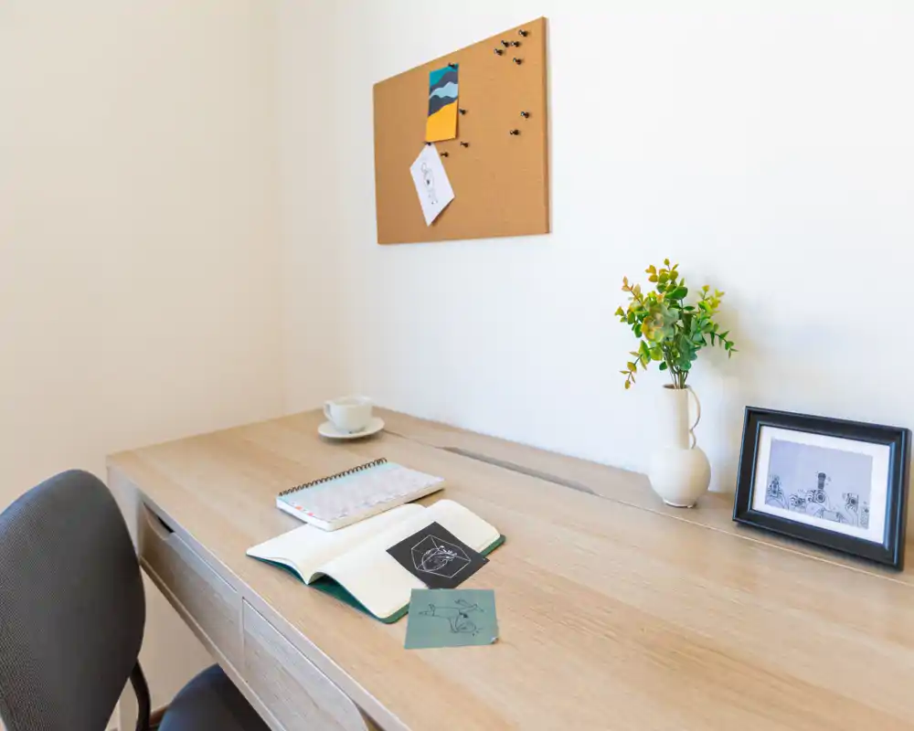 Área de trabajo luminoso y minimalista con escritorio de madera, silla, panel de corcho y pequeños objetos decorativos — ideal para trabajo remoto o estudio.