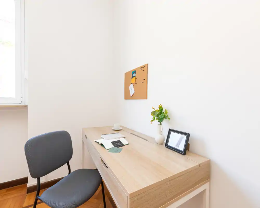 Rincón de trabajo luminoso y minimalista con escritorio de madera, silla sencilla, corcho y pequeño jarrón decorativo — ideal como oficina en casa o zona de estudio.