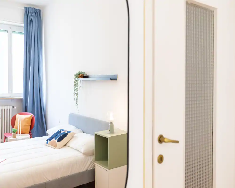 Dormitorio luminoso y bien presentado con cama doble arreglada, textiles suaves, lámpara de mesita y ventana que aporta luz natural.