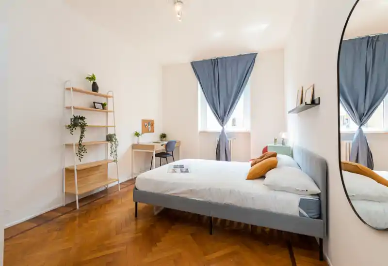 Dormitorio luminoso y con estilo con cama grande tapizada, suelo de parqué, escritorio junto a la ventana y decoración cuidada — perfecto para estancias cómodas.