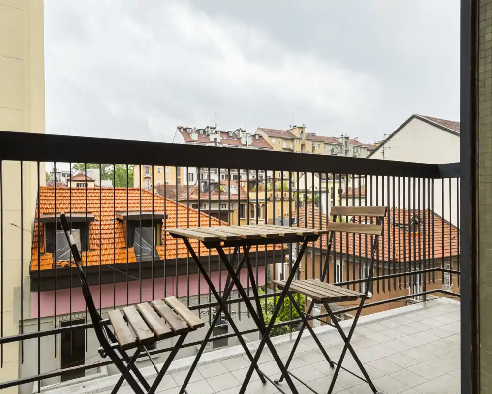 Balcon avec une petite table bistro en bois et deux chaises pliantes, donnant sur des toits en terre cuite — parfait pour un café le matin ou une soirée tranquille.