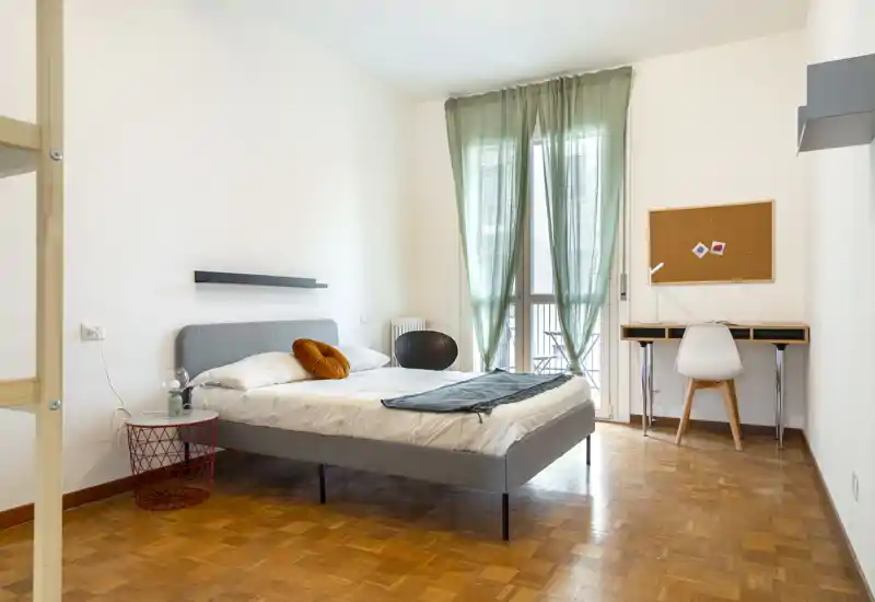 Camera da letto moderna e luminosa con letto matrimoniale ben rifatto, tessili accoglienti e una scrivania vicino alla finestra che lascia entrare luce naturale.