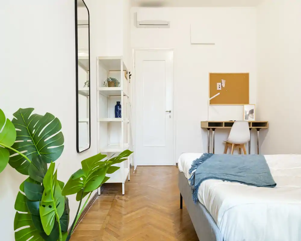 Dormitorio luminoso y minimalista con cama bien hecha, escritorio pequeño y planta decorativa: ideal para una persona o estudiante.