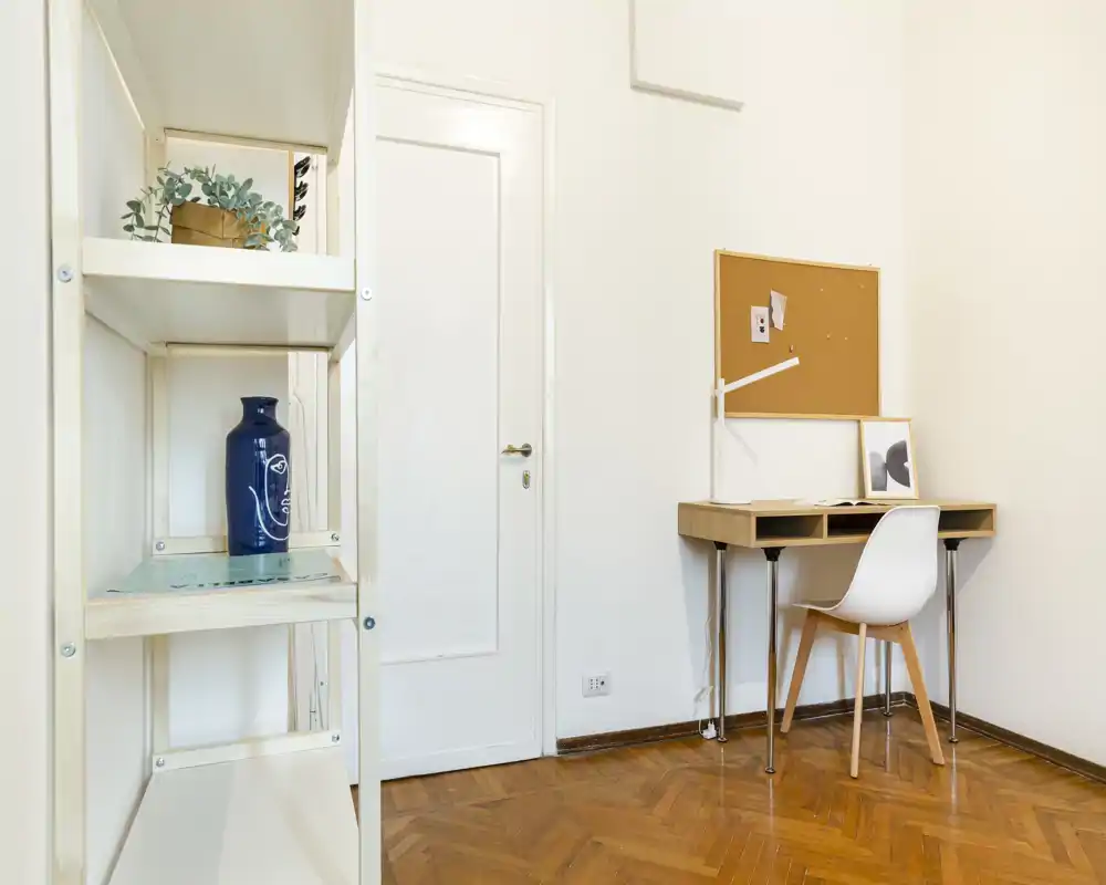 Rincón living/trabajo minimalista con un pequeño escritorio, silla y estantería; paredes neutras y suelo de madera cálido que crean un espacio funcional y tranquilo.