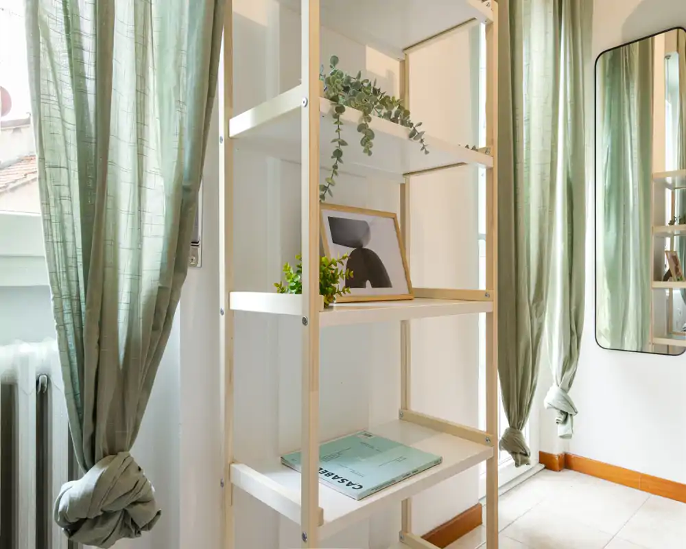 Rincón luminoso de la sala con una estantería alta, un cuadro enmarcado y cortinas verdes que armonizan el espacio.