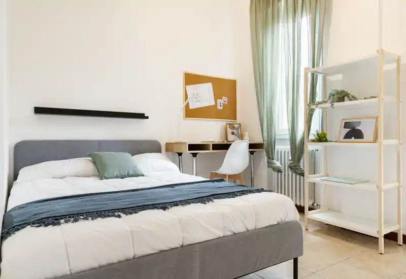 Camera da letto luminosa e ben arredata con letto matrimoniale ordinato, tessili morbidi e una piccola postazione di lavoro vicino alla finestra per un ambiente accogliente.