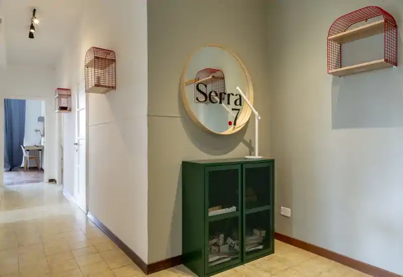 Neat entrance/hallway with decorative shelving, a round mirror and a compact green storage cabinet — well lit and styled for a welcoming first impression.