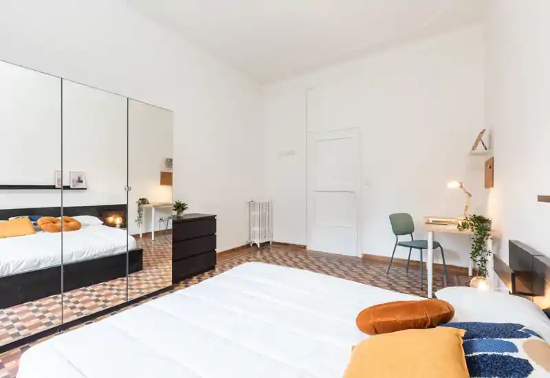 Dormitorio amplio y luminoso con cama doble cómoda, suelo de mosaico y un gran armario con espejo que aporta profundidad. Un pequeño escritorio y cojines cálidos crean un ambiente acogedor.