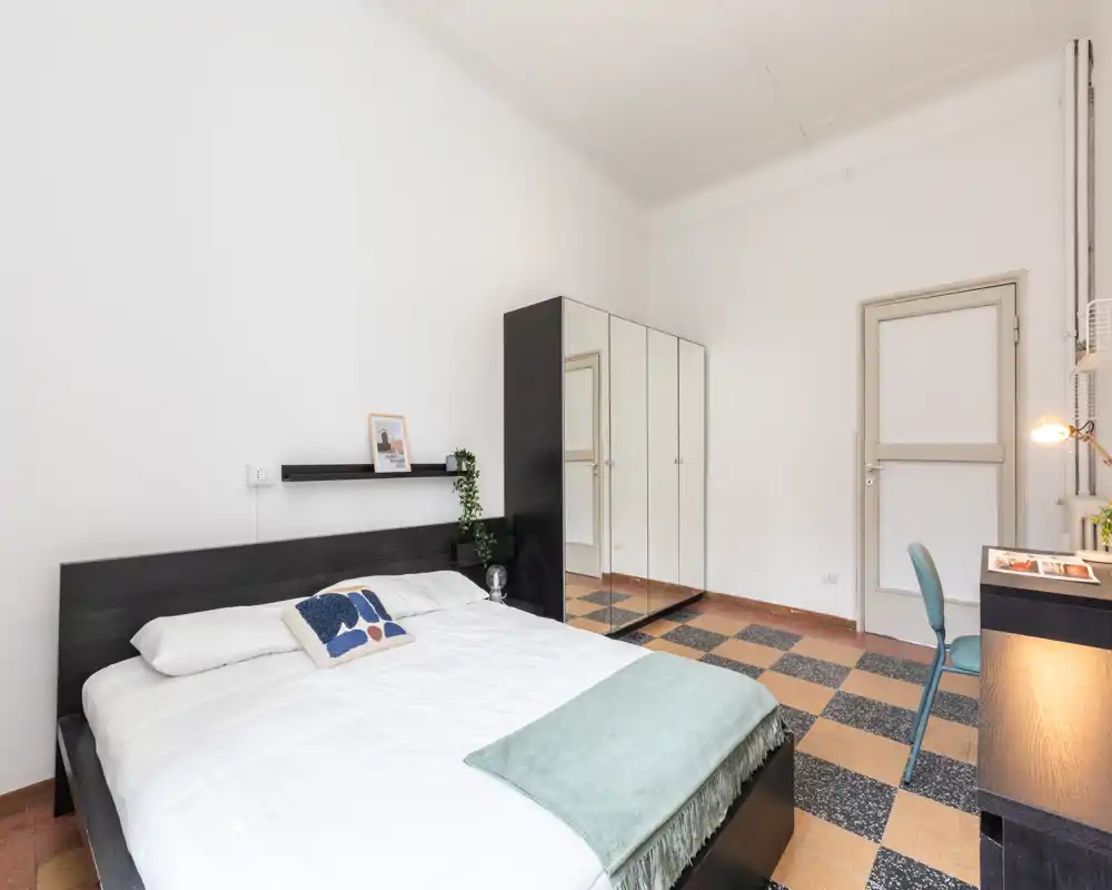 Dormitorio luminoso y moderno con cama doble grande, armario con puertas espejo y pequeño escritorio; estilo minimalista y ordenado, perfecto para anuncios de alquiler.