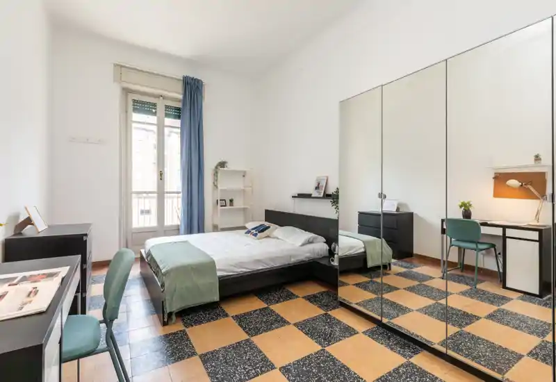 Dormitorio luminoso y bien decorado con cama doble, amplio armario con espejo y rincón de estudio junto a la ventana. La luz natural y la paleta limpia hacen la habitación acogedora y funcional para descansar y trabajar.