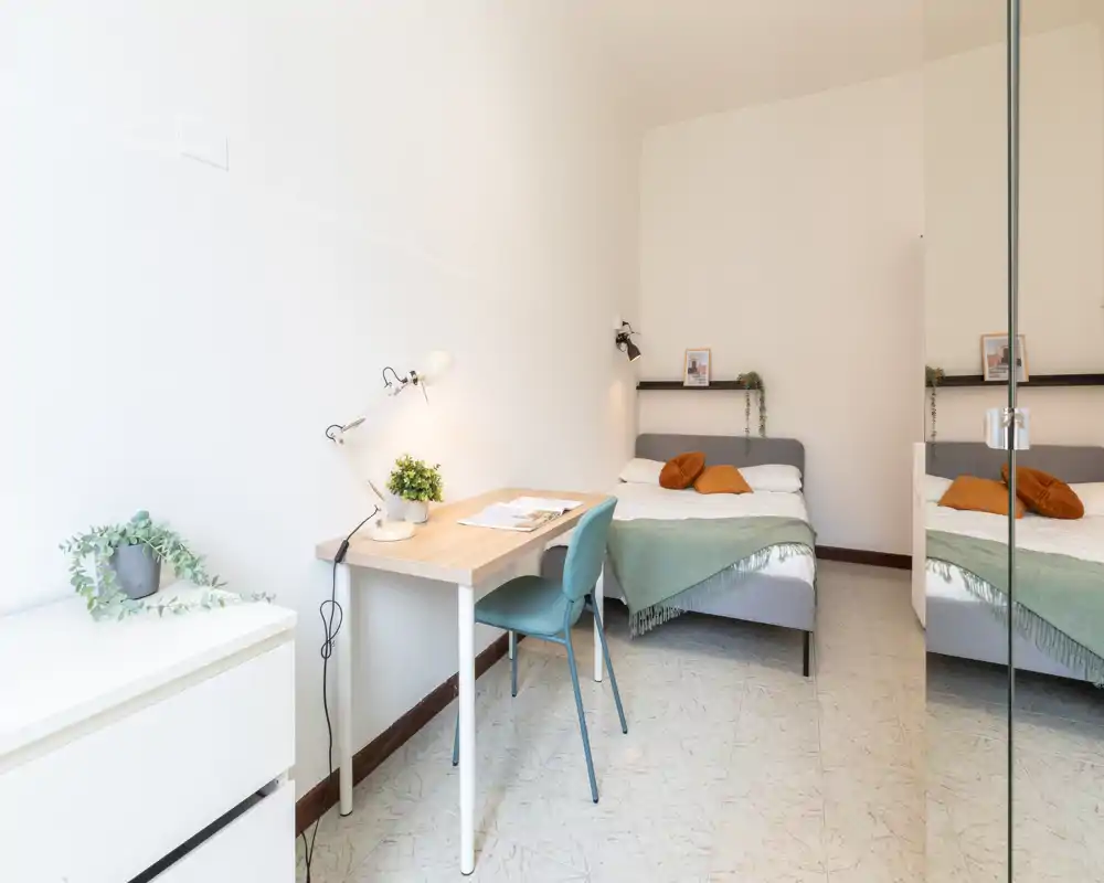 Chambre lumineuse et moderne avec un lit double, plaid vert et coussins chauds, ainsi qu'un petit bureau contre le mur — parfaite pour une personne ou un couple recherchant un espace minimal et lumineux.