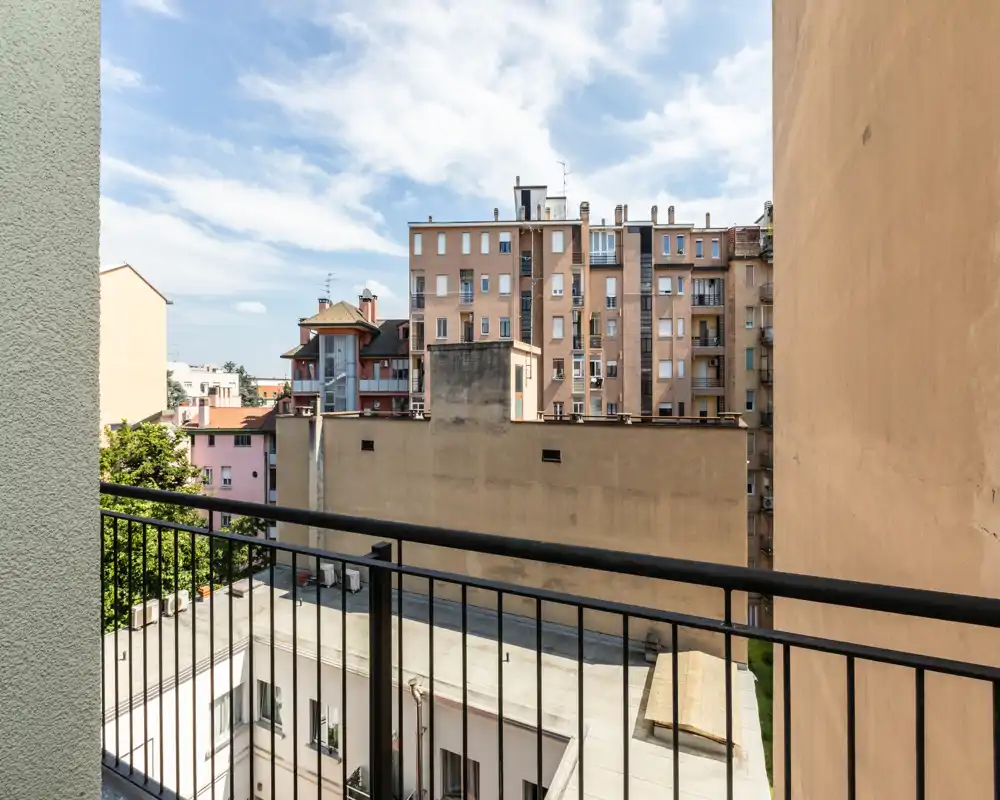 Balcon offrant une vue sur les immeubles voisins et la cour, garde-corps métallique au premier plan et ciel bleu dégagé.