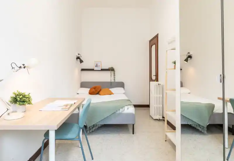 Chambre lumineuse et minimaliste avec lit double, lampes de chevet et petit bureau. Textiles doux et coussins chauds pour une ambiance accueillante.