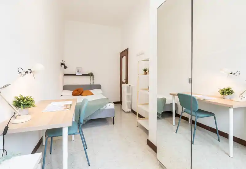 Chambre lumineuse et épurée avec lit double, coussins confortables et bureau, agrandie visuellement par une grande armoire miroir.