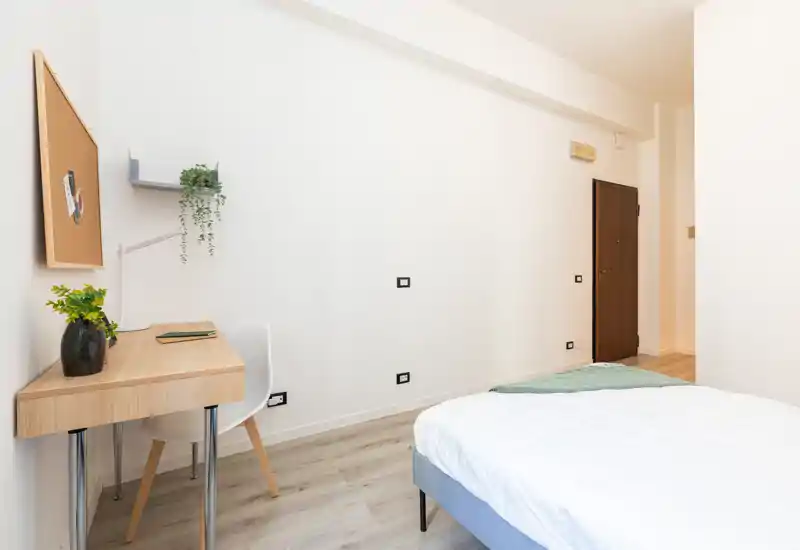 Bright, modern bedroom with a neatly made bed, simple desk and light wood flooring — ideal for a single occupant or student.