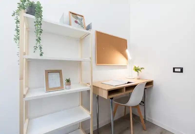 Bright, minimal home office nook with a wooden desk, chair, corkboard and shelving — ideal for studying or remote work.