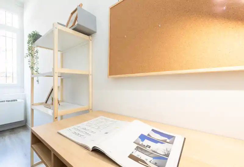 Bright, minimal workspace corner with a wooden desk, open shelving and a cork noticeboard — ideal for study or remote work.