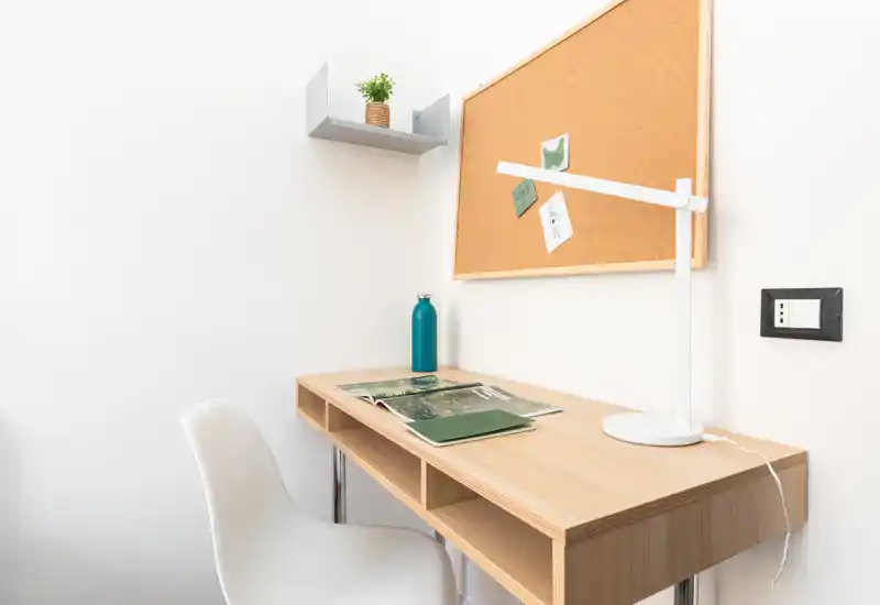 Compact study corner with a wooden desk, white chair, desk lamp and cork bulletin board — bright and minimally styled workspace ideal for reading or remote work.