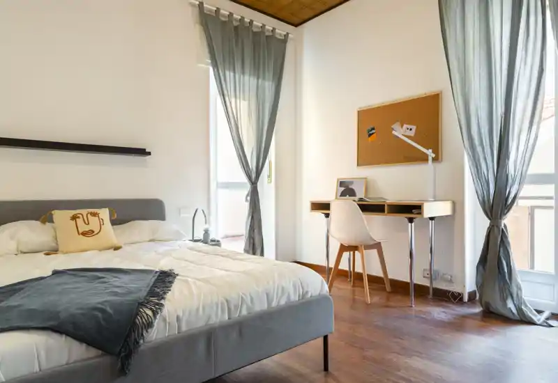 Bright, modern bedroom with a comfortable double bed, soft linens, and a small study desk by the window letting in abundant natural light.