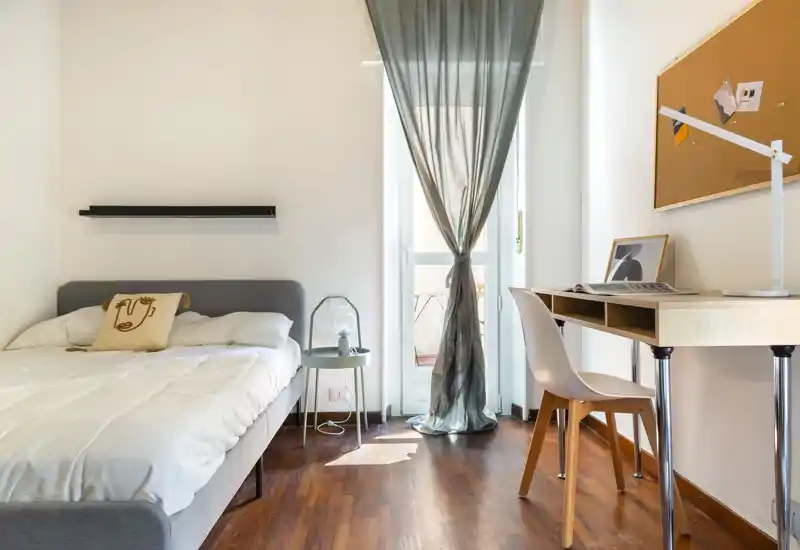 Bright, modern bedroom with a comfortable double bed, bedside table and a desk by the window letting in natural light.