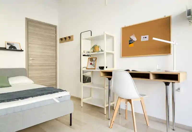 Dormitorio moderno y luminoso con cama bien hecha, escritorio funcional y estantería: ideal para estudiantes o profesionales que buscan un espacio ordenado y bien iluminado.
