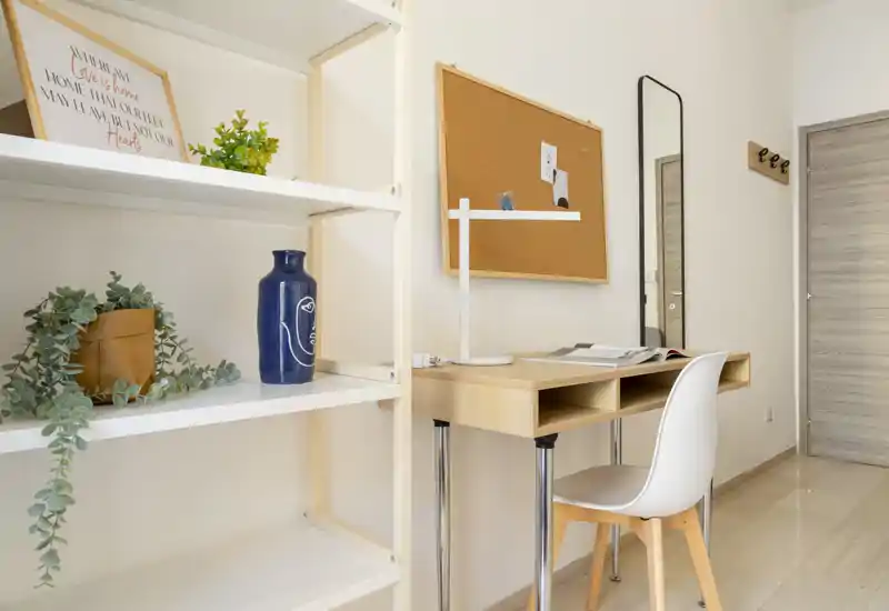 Rincón de estudio luminoso y minimalista con escritorio de madera, silla blanca y estanterías decorativas — ideal para teletrabajo o lectura.