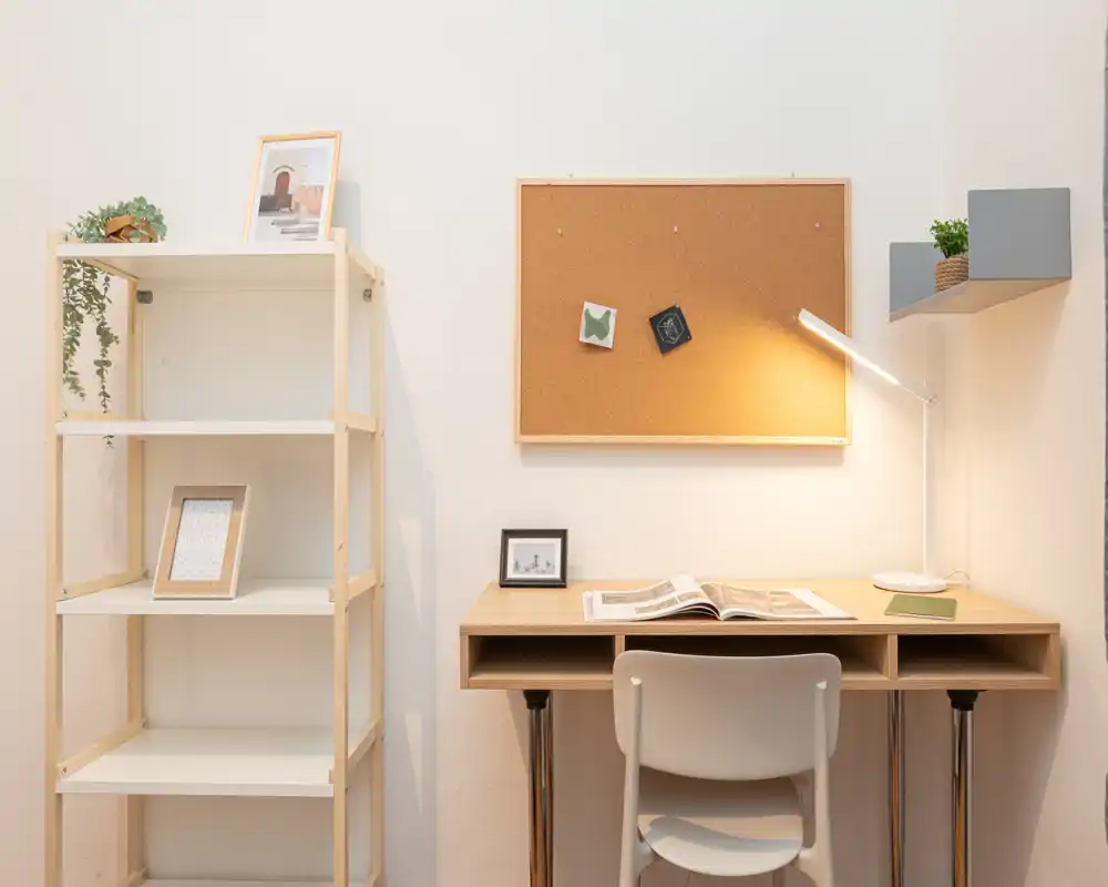 Bright, minimal study corner with a wooden desk, chair, corkboard and task lamp — a neat workspace ideal for remote work or studying.
