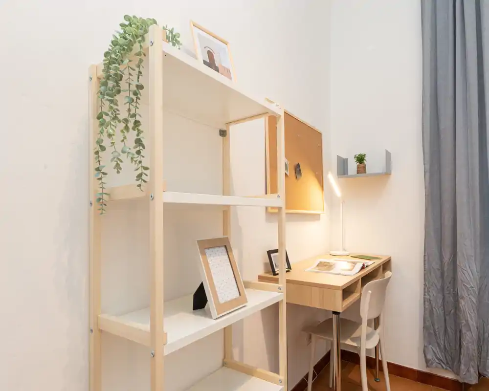 Small study / living nook with a wooden desk, chair, shelving and a desk lamp — tidy and simply decorated, suitable for remote work or reading.