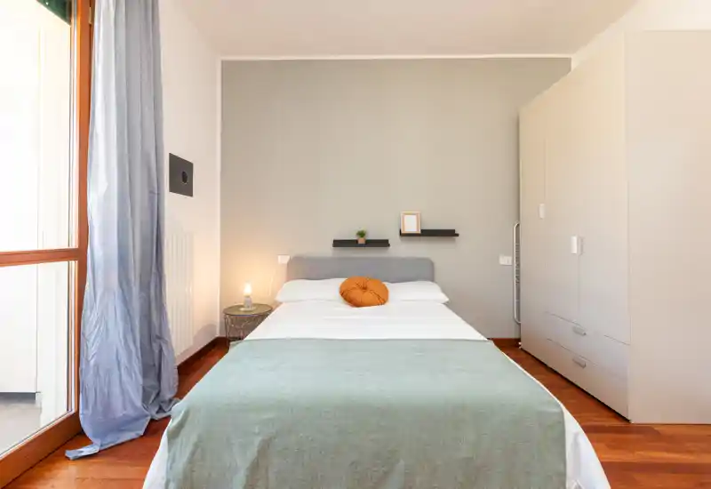 Chambre lumineuse et soignée avec lit double, table de chevet et armoire ; jeté vert et coussin décoratif apportent une atmosphère chaleureuse.