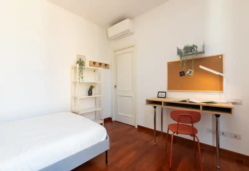 Chambre simple lumineuse et bien aménagée avec lit confortable, sol en bois, bureau et étagères — idéale pour un étudiant ou une personne seule.
