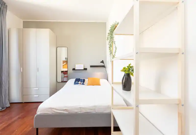 Chambre moderne et lumineuse avec un lit double bien fait, parquet en bois et une armoire indépendante. Décor minimaliste, plantes et lumière naturelle pour une atmosphère accueillante idéale pour une annonce.