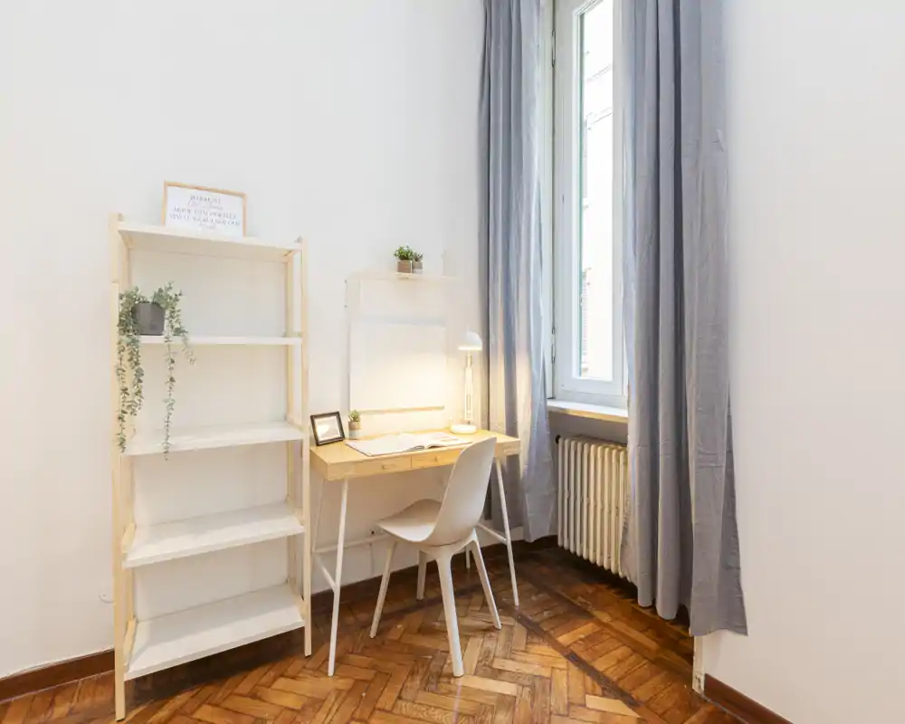 Angolo luminoso e minimale con scrivania in legno, sedia e scaffale accanto a una grande finestra: ideale come spazio studio o postazione lavoro in camera.