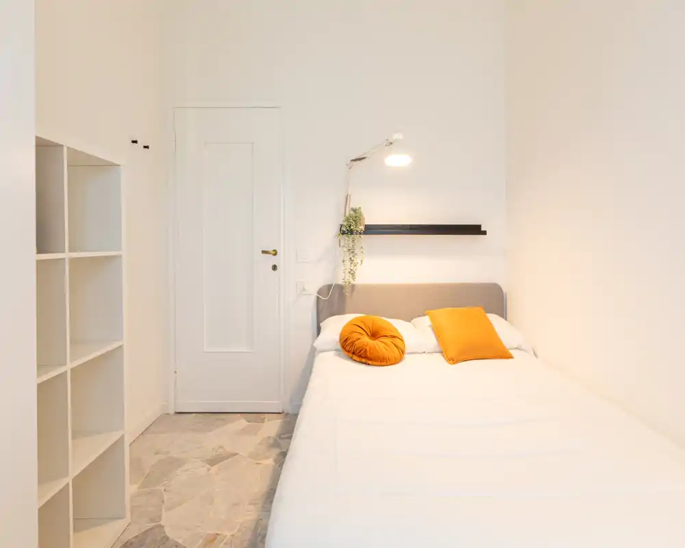 Camera da letto luminosa e minimal con letto matrimoniale, cuscini caldi e lampada da lettura — ideale per un soggiorno accogliente per una o due persone.