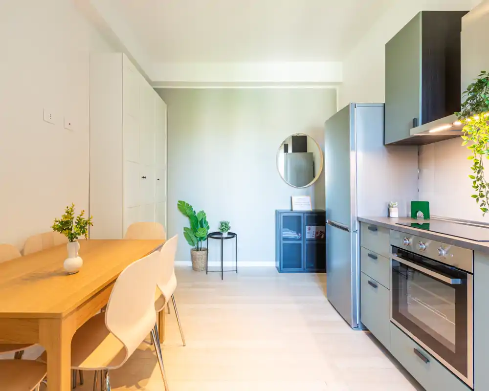 Cucina open-space moderna con tavolo in legno, sedie e elettrodomestici incassati; ambiente luminoso, elegante e accogliente perfetto per pranzi in piccolo gruppo.