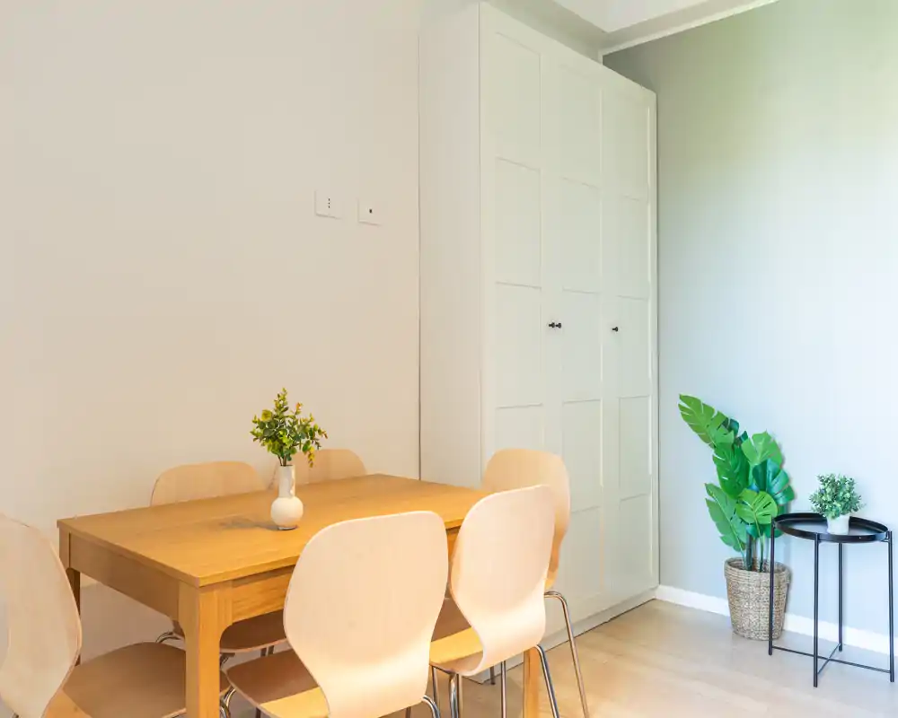 Zona pranzo luminosa e minimale con tavolo in legno, sedie chiare e piante decorative che creano un'atmosfera moderna e accogliente.