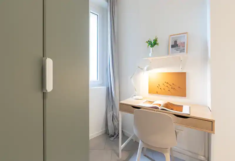 Espace de travail lumineux et compact avec bureau en bois, chaise, lampe et tableau en liège près d'une fenêtre — un coin bureau minimaliste et apaisant.