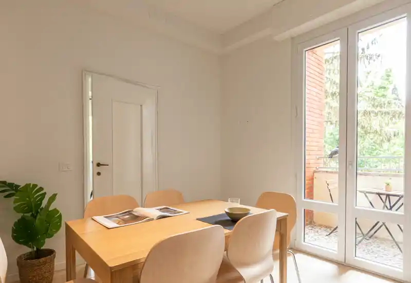 Coin repas lumineux et minimaliste avec une table en bois, quatre chaises et une belle lumière naturelle provenant des grandes portes-fenêtres donnant sur le balcon.