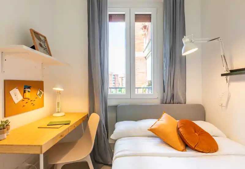 Camera da letto luminosa e compatta con letto comodo, cuscini caldi e una piccola scrivania vicino alla finestra — pulita, luminosa e arredata con gusto per soggiorni brevi.