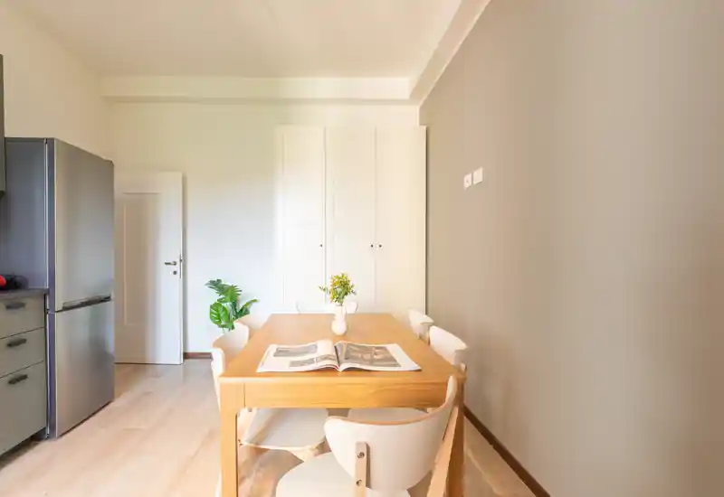 Coin repas ensoleillé avec table en bois et quatre chaises modernes, agrémenté d'un petit vase et d'un magazine ouvert — style minimaliste et soigné, idéal pour les annonces immobilières.